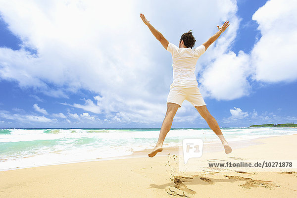 'Mann  der am Strand in die Luft springt; Kealia  Kauai  Hawaii  Vereinigte Staaten von Amerika'.