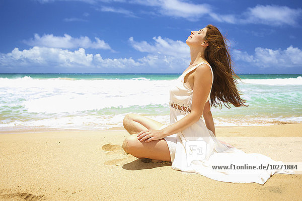 Eine Frau  die im Sand am Ufer des Wassers sitzt und die Sonne genießt; Kealia  Kauai  Hawaii  Vereinigte Staaten von Amerika'.