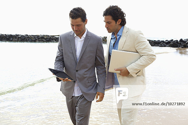 'Businessmen walking with tablet and laptop at the water's edge  Lydgate Beach; Kauai  Hawaii  United States of America'