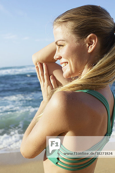 Junge Frau in Fitnesskleidung steht am Strand am Rande des Wassers; Kauai  Hawaii  Vereinigte Staaten von Amerika'.
