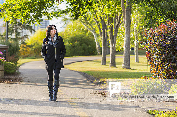 'Mature businesswoman walking outdoors in a city park in autumn; Edmonton  Alberta  Canada'