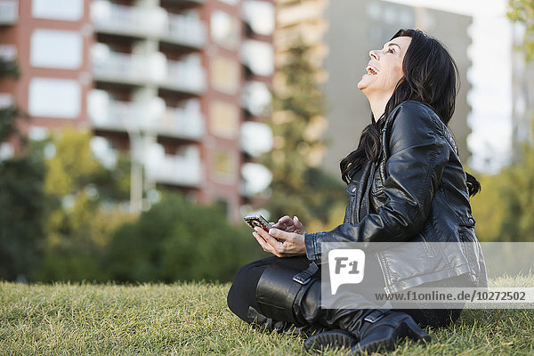 Ältere Frau lacht über eine Nachricht auf ihrem Smartphone in einem städtischen Park im Herbst; Edmonton  Alberta  Kanada'.
