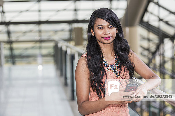 'Young professional businesswoman holding a smart phone in lobby of office building; Edmonton  Alberta  Canada'