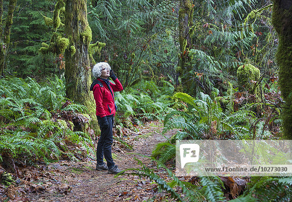 'A mature woman on a cell phone hiking in the rainforest in the Cowichan Valley; British Columbia  Canada'