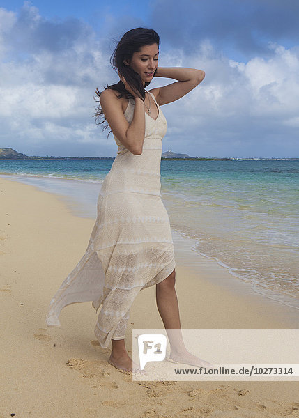 'Young woman in white dress on the beach at the water's edge; Kailua  Island of Hawaii  Hawaii  United States of America'