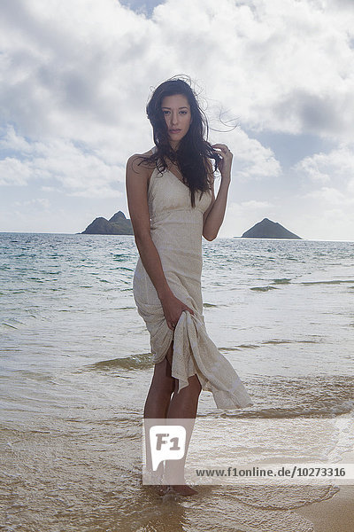 'Young woman in white dress on the beach at the water's edge; Kailua  Island of Hawaii  Hawaii  United States of America'