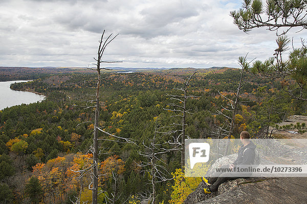 'Man sitting on the edge of a cliff atop Booth's Rock with a view of Rock Lake  Algonquin Park; Ontario  Canada'