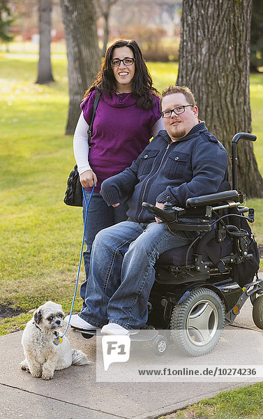 'Disabled husband with his wife and their pet dog posing for a family portrait in a park in autumn; Edmonton  Alberta  Canada'