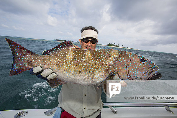 'Fisherman holding a fresh caught Grouper (Epinephelinae); Tahiti'