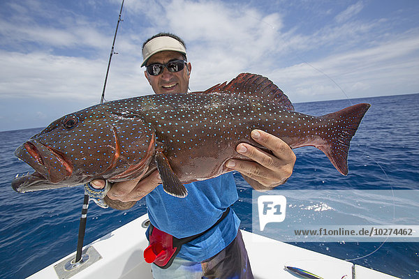 'Fisherman holding a fresh caught Grouper (Epinephelinae); Tahiti'
