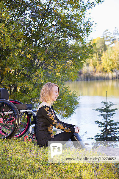 'Young disabled woman sitting beside her wheelchair in a city park in autumn; Edmonton  Alberta  Canada'