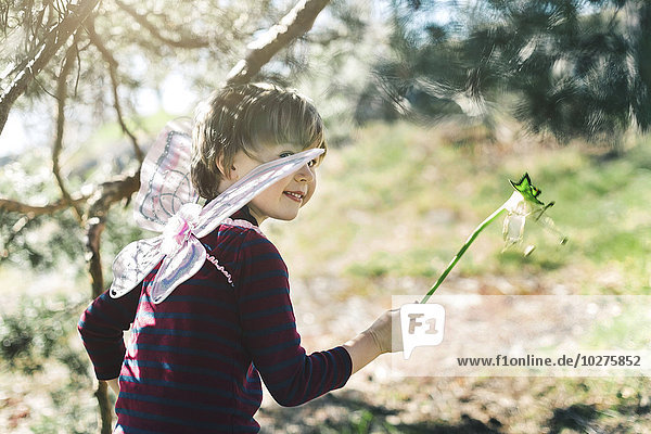 Smiling boy in fairy wings looking away at yard