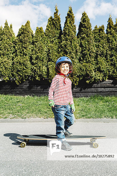 Porträt eines selbstbewussten Jungen mit Skateboard auf dem Gehweg am Hof