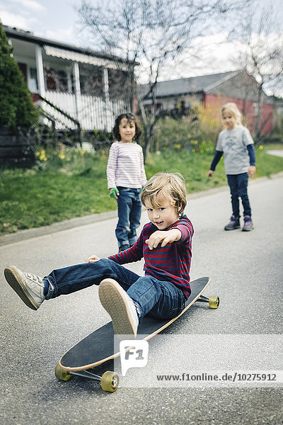 Kinder beim Betrachten des Freundes Skateboard auf dem Fußweg vor dem Haus