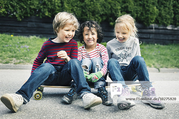 Playful friends sitting on skateboard at yard