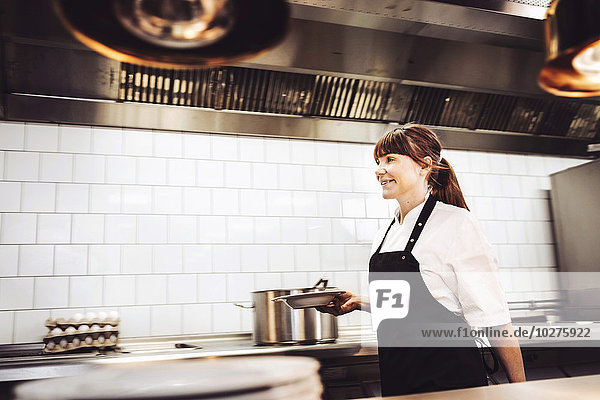 Kvinnlig kock går med tallrik genom restaurangkök