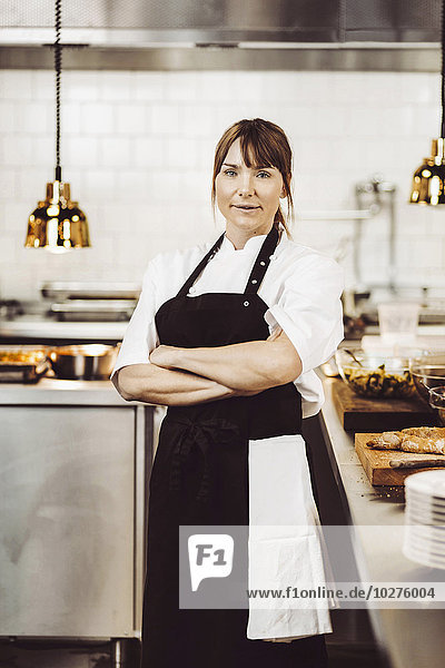 Porträt einer selbstbewussten Köchin  die in der Großküche die Arme gekreuzt hat.