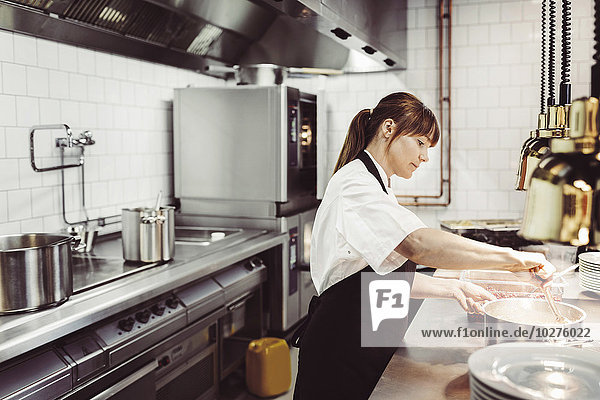 Side view of female chef preparing dish in commercial kitchen