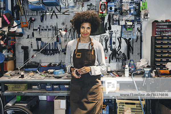 Portrait of confident female mechanic holding bicycle gear in workshop
