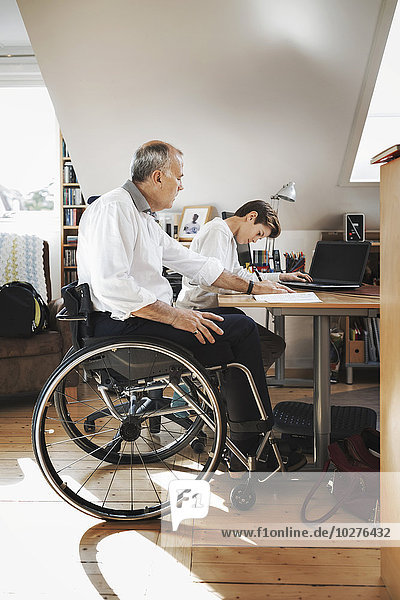 Side view of disabled man looking at son studying at home