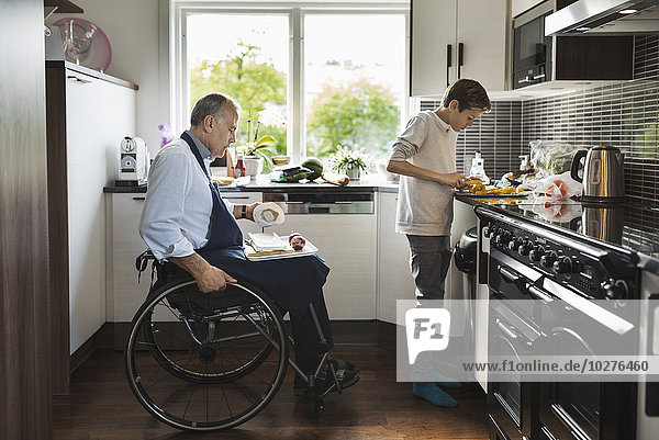 Son with disabled father cutting vegetables in kitchen