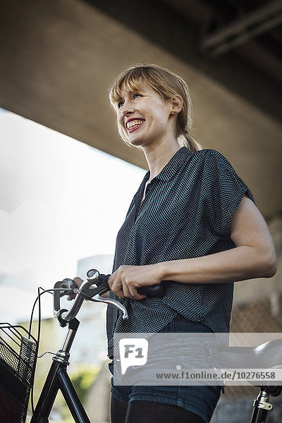 Happy businesswoman with bicycle looking away while standing under bridge