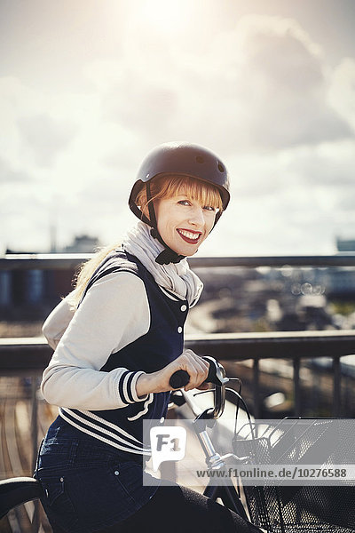 Side view portrait of happy businesswoman standing with bicycle on bridge