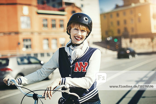 Porträt einer glücklichen Frau  die mit dem Fahrrad auf der Stadtstraße steht.
