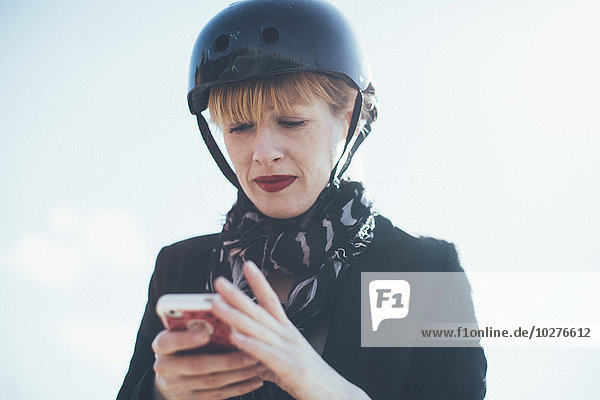 Niederwinkelansicht der Geschäftsfrau im Fahrradhelm mit Handy gegen den Himmel