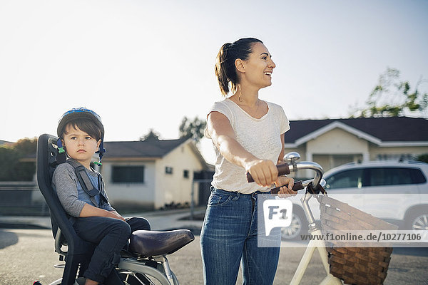 Glückliche Frau schaut weg  während ihr Sohn auf dem Fahrrad sitzt.