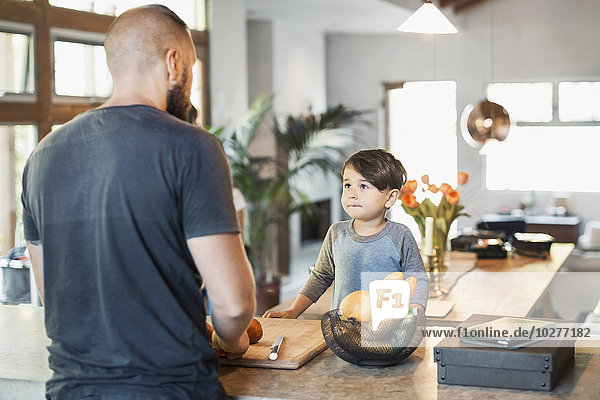 Boy looking at father standing at kitchen counter