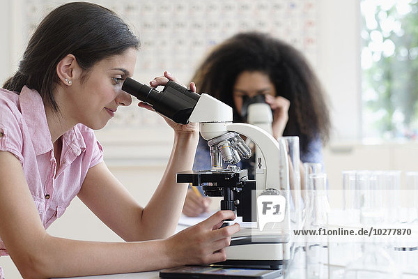 Mädchen im Teenageralter (14-15  16-17) bei der Verwendung eines Mikroskops im naturwissenschaftlichen Unterricht