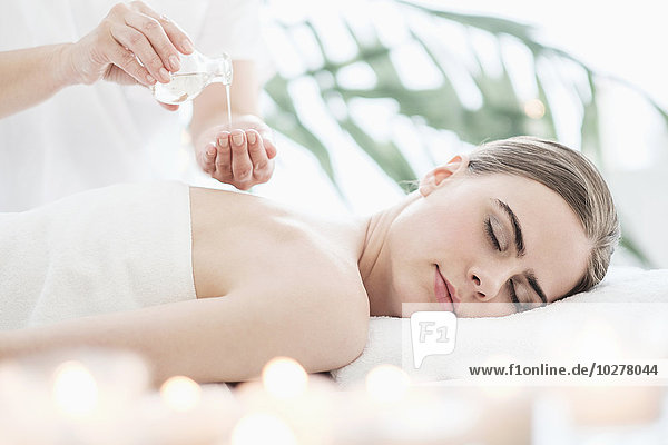 Therapist putting massaging oil on young woman in spa
