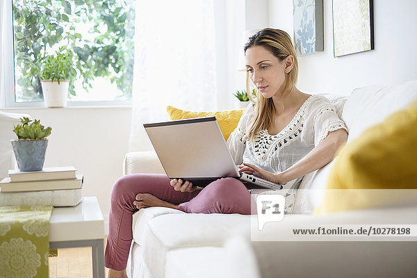 Woman with laptop sitting on sofa