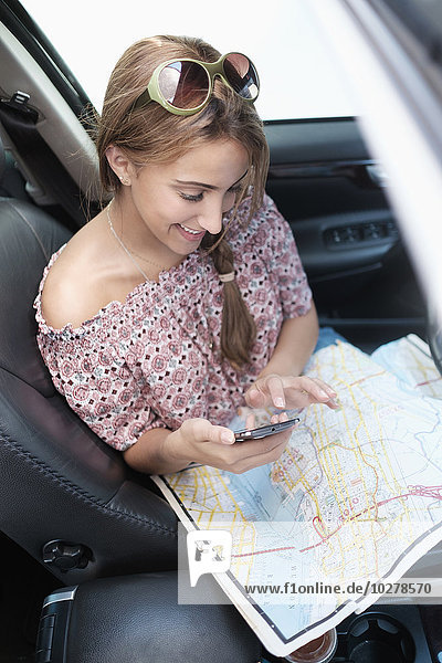 Frau überprüft Telefon im Auto mit Karte auf dem Schoß