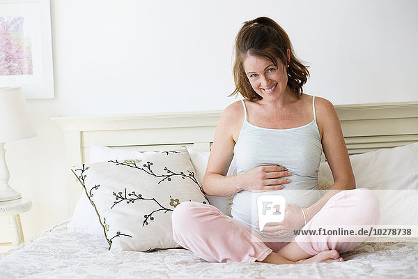 Lächelnde schwangere Frau auf dem Bett sitzend