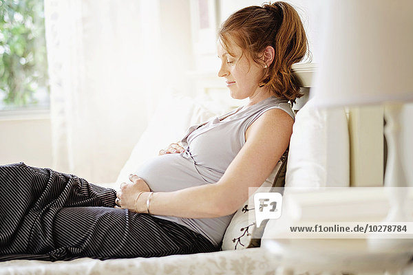 Smiling pregnant woman sitting on bed