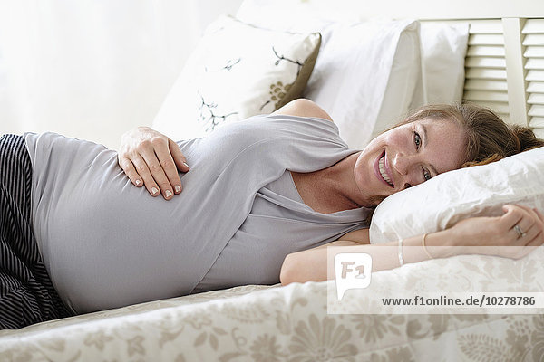 Lächelnde schwangere Frau auf dem Bett liegend