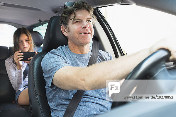 Mann fährt Auto  Mädchen (10-11) schreibt im Hintergrund eine SMS