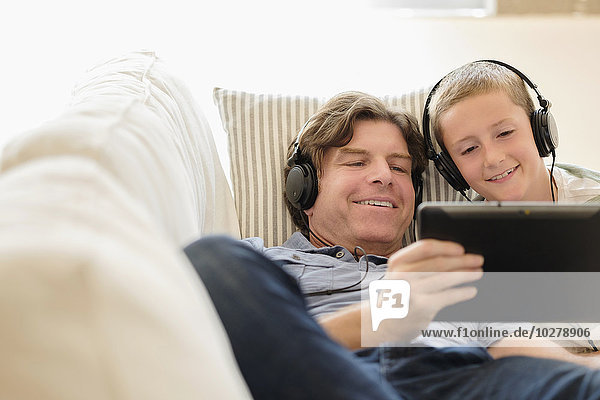 Man using tablet pc with his son (8-9) on sofa