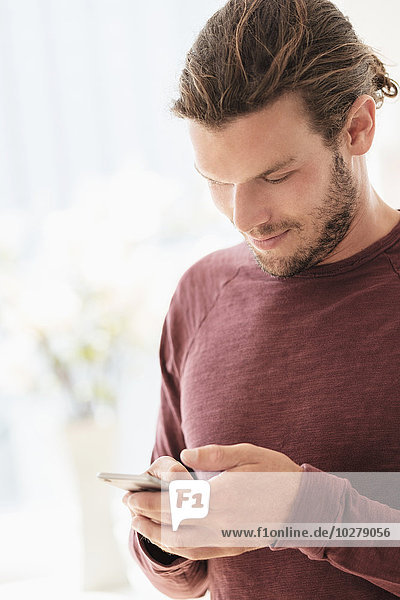 Ein Mann im mittleren Erwachsenenalter schreibt eine SMS in einem Haus