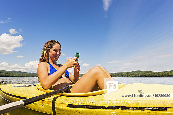 Junge Frau benutzt Smartphone im Kajak auf dem See