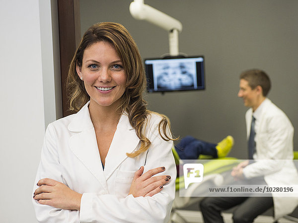 Porträt eines Zahnarztes mit einem Kollegen und einem Patienten (8-9) im Hintergrund