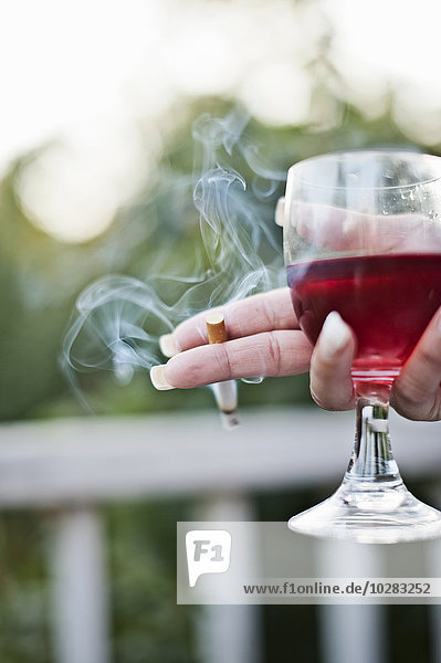 Eine Frau hält eine Zigarette und ein Glas Wein in der Hand