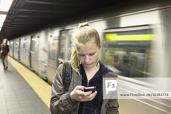 Junge Frau schaut auf ihr Smartphone  Zug im Hintergrund