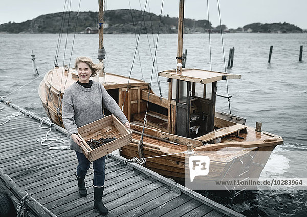 Lächelnde Frau mit Hummern  Boot im Hintergrund
