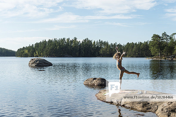 Mädchen steht auf einem Felsen am See