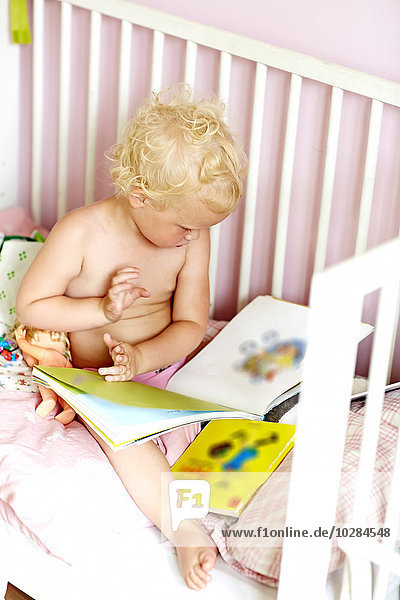 Mädchen im Kinderbett schaut sich Bücher an