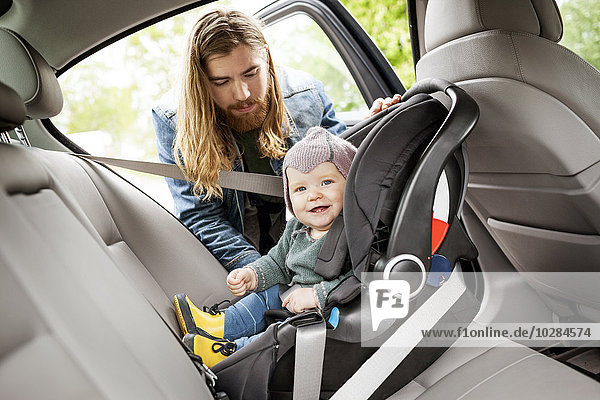 Vater setzt Baby in Autositz