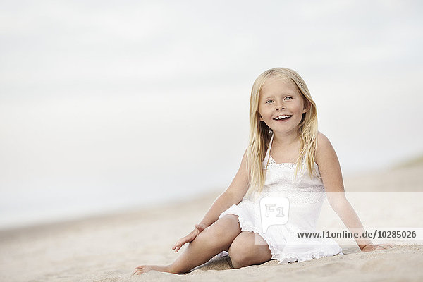 Lächelndes Mädchen am Strand sitzend